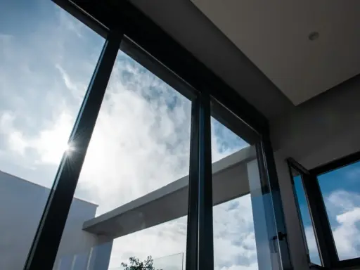 El sol brilla a través del vidrio guardian, iluminando un cielo azul con nubes blancas.