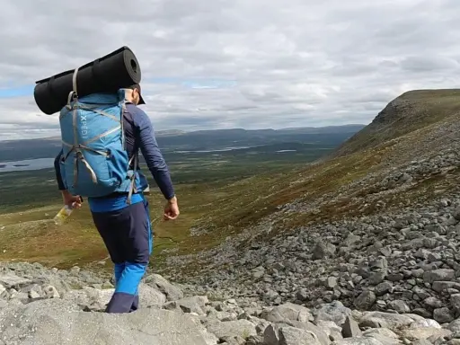 Vandrare med ryggsäck och liggunderlag på väg nerför en stenig fjällsida. En perfekt packlista vandring för äventyret.