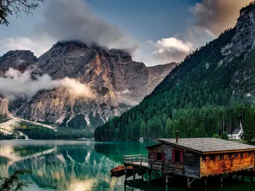 Lago alpino con baita in legno e montagne nebbiose. Curiosità sul Trentino Alto Adige: un luogo da fiaba.