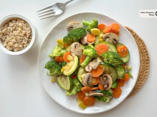 Un colorido salteado de verduras con brócoli, zanahoria, calabacín y champiñones, servido junto a un tazón de arroz integral.