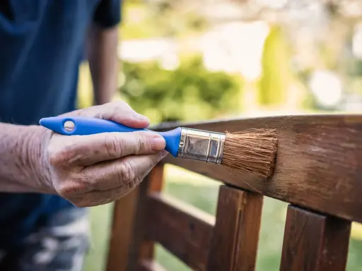 Mano aplicando barniz a un banco de jardín, creando un hermoso efecto madera.