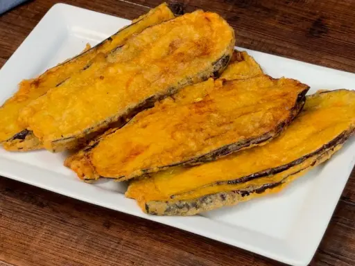 Fette di melanzane fritte, dorate e croccanti, servite su un piatto bianco. Un assaggio delle deliziose melanzane alla pullastiello.