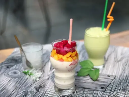 Pyszny koktajl białkowy z kawałkami smoczego owocu i mango. Obok zielony smoothie i szklanka z lodem.