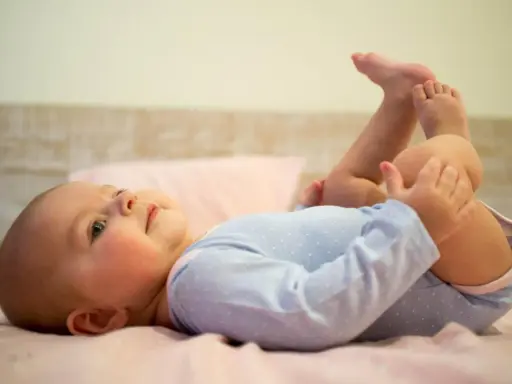 5-miesięczne dziecko leży na plecach, podnosząc nóżki i bawiąc się nimi. To pokazuje, co potrafi 5 miesięczne dziecko.