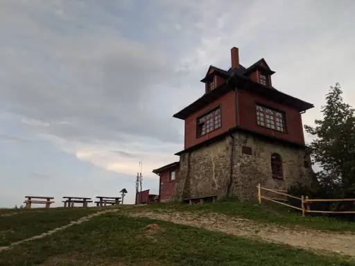 Drewniana wieża widokowa na Luboniu Wielkim, z kamiennym fundamentem, otoczona zielenią i ławkami.