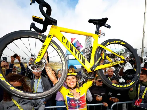 Jubelnde Radfahrerin hebt ihr gelbes Canyon-Rennrad hoch. Ein Moment des Triumphs bei der Frauen Tour de France.