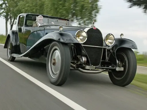 Ein Mann fährt einen glänzenden schwarzen Bugatti Royale auf einer Landstraße. Der Bugatti Royale Preis ist astronomisch, ein Traum für jeden Sammler.