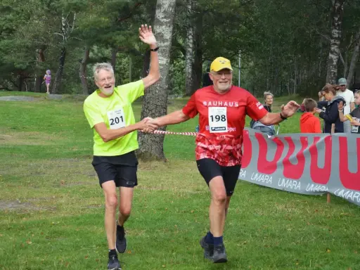 Två glada löpare, nummer 201 och 198, skakar hand vid målgången på kåsjön trail.