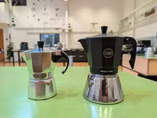Zwei Espressokocher, ein silberner und ein schwarzer, stehen bereit für den perfekten Espresso auf dem Herd.