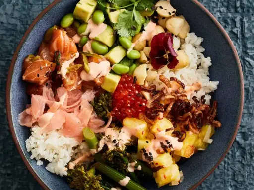 Eine bunte Poke Bowl mit Lachs, Avocado, Edamame, Reis, eingelegtem Ingwer und knusprigen Zwiebeln.