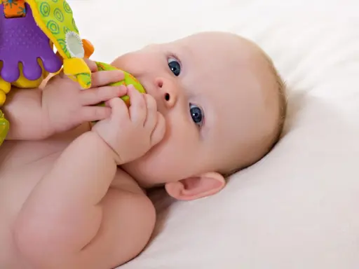 Ein Baby mit blauen Augen erkundet sein buntes Spielzeug. Vielleicht ist es der 19-Wochen-Schub, der ihn so neugierig macht.