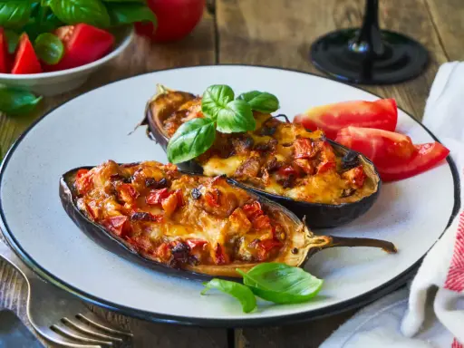 Melanzane ripiene senza carne, dorate e filanti, guarnite con basilico fresco e pomodoro. Un piatto vegetariano invitante.