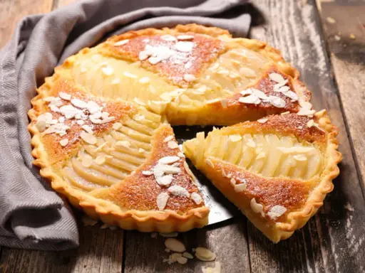 Une délicieuse tarte aux poires, garnie d'amandes effilées et saupoudrée de sucre glace, repose sur un plateau en bois.
