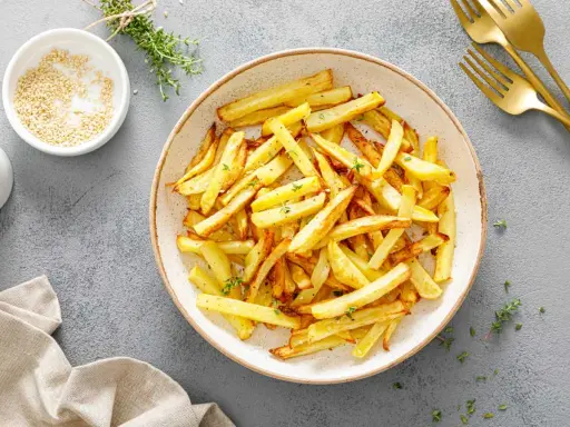 Un plato lleno de crujientes patatas fritas doradas, espolvoreadas con hierbas frescas. ¡Perfectas para compartir!