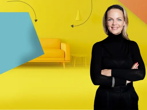 Frau mit Armen verschränkt vor gelbem Hintergrund mit Sofa und Beistelltisch. Inspiration für Renovierungs Serien Deutsch.