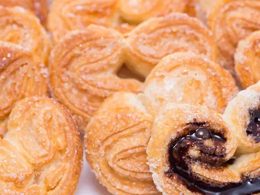 Deliciosas palmeritas de hojaldre espolvoreadas con azúcar. Algunas tienen un relleno de chocolate oscuro y brillante.
