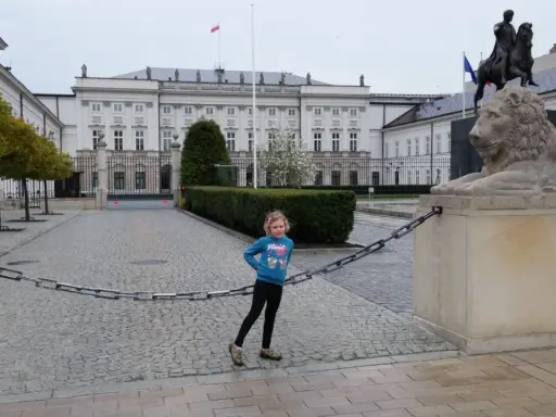 Dziewczynka na trasie traktu królewskiego w Warszawie, obok lwa i pomnika konnego.