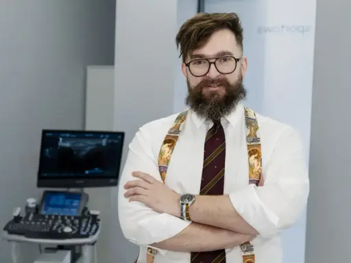 Ortopeda w okularach i ozdobnych szelkach stoi przed aparatem USG.