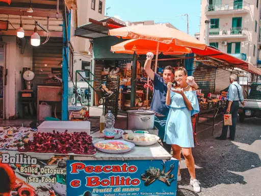 Coppia felice assaggia polpo fritto in un mercato di Palermo in un giorno di sole. Un assaggio autentico della Sicilia.
