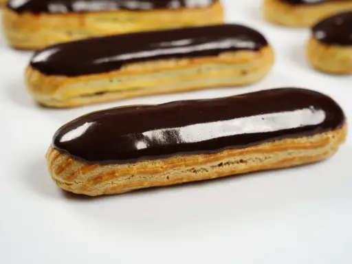 Plusieurs éclairs au chocolat brillants, avec un fondant pour éclair parfait, sont disposés sur fond blanc.