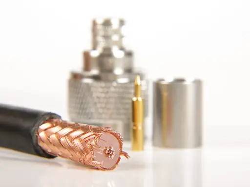Przewód ekranowany z miedzianym oplotem, obok złoty pin i metalowe złącza.