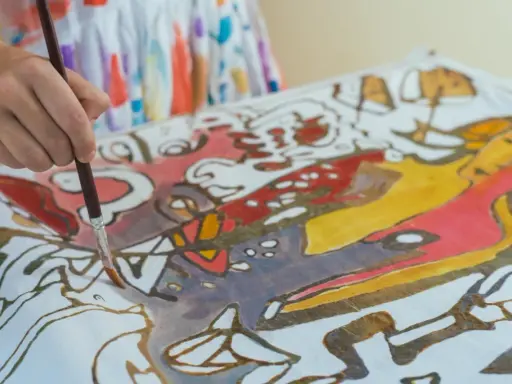 Ręka maluje pędzelkiem wzory na tkaninie, tworząc barwny obraz w technice papatya batik.