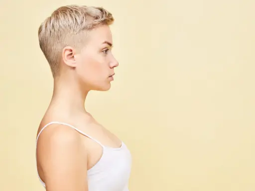 Perfil de una mujer joven con un moderno corte pixie rubio, luciendo un top blanco.