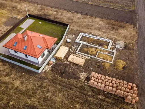Działka rolno budowlana z gotowym domem i fundamentami pod kolejny. Materiały budowlane czekają na rozpoczęcie prac.