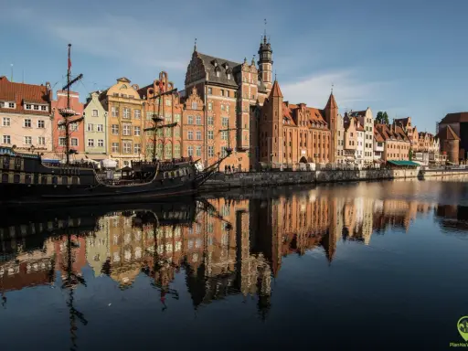 Gdańsk atrakcje: zabytkowy żaglowiec cumuje przy Motławie, w tle kolorowe kamienice i Żuraw. Odbicia budynków w wodzie.