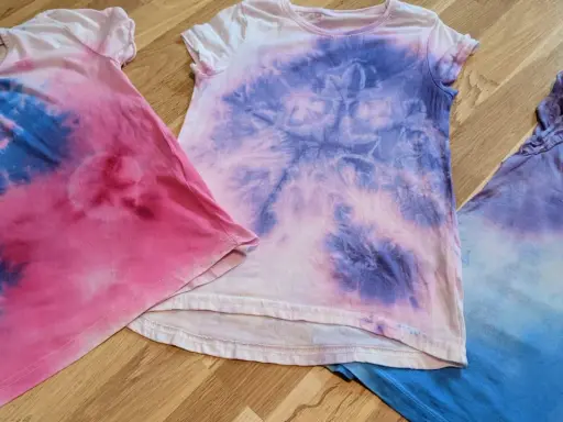 Batik mit Kindern: Drei bunte T-Shirts in Rosa, Lila und Blau, die nach einem kreativen Nachmittag aussehen.