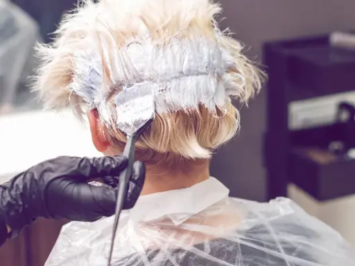 Friseur mit Handschuhen trägt Bleichmittel auf blondes Haar auf. Der Prozess des Haare bleichen beginnt.
