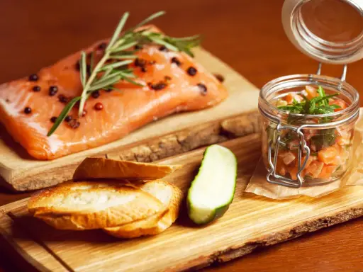 Świeży łosoś z rozmarynem i pieprzem, tartare w słoiczku, pieczywo i ogórek. Zdrowe łosoś kcal na drewnianej desce.