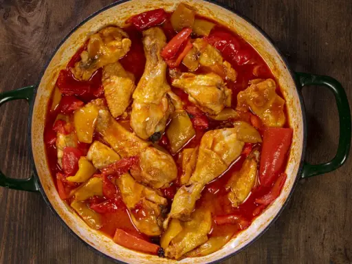 Un saporito pollo con peperoni in umido, cotto in una casseruola verde su un tavolo di legno scuro.
