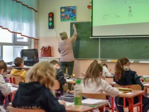 Nauczycielka dyplomowana pisze na tablicy, dzieci słuchają. Ciekawe, jakie nauczyciel dyplomowany zarobki ma w tej szkole.