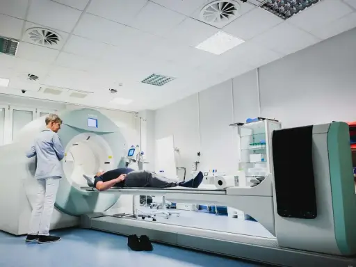 Pacjent leży na stole aparatu do tomografii komputerowej, nadzorowany przez technika.