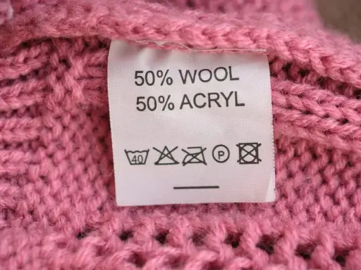 Tvättråd på en rosa stickad tröja: 50% ull, 50% akryl. Kan indikera nackdelar med ull som känslighet för höga temperaturer.