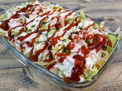 Kapsalon z kurczakiem, sałatą, pomidorami, ogórkiem i sosami w szklanej misce.