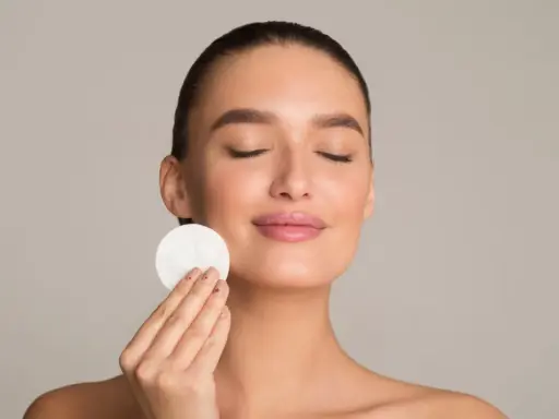 Donna con occhi chiusi applica un dischetto di cotone sul viso, parte della sua routine di skincare viso per una pelle radiosa.