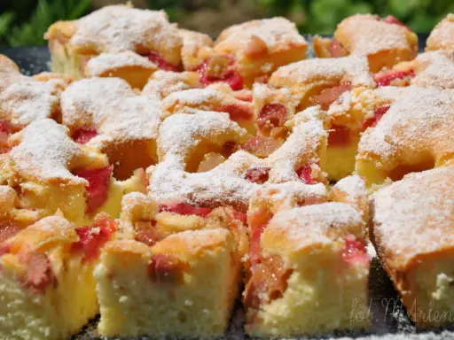 Pyszne ciasto z rabarbarem, pokrojone na kwadraty i posypane cukrem pudrem. Idealne na letnie popołudnie.