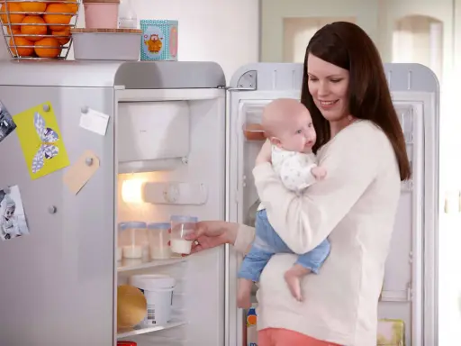 Mama z dzieckiem przy lodówce, gdzie przechowywanie mleka matki jest łatwe dzięki specjalnym pojemnikom.
