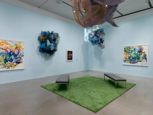 Abstract paintings and fabric sculptures adorn the walls of the Lanoue Gallery, with benches placed on a patch of artificial grass.