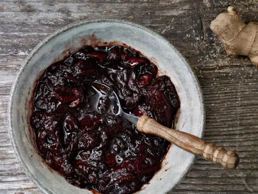 Dunkles, glänzendes Zwetschgen-Chutney in einer Schale, daneben ein Stück Ingwer und Zucker.