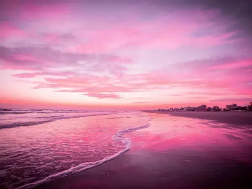 Spiaggia di Riccione immersa nel rosa della Notte Rosa, con il mare calmo e il cielo infuocato.