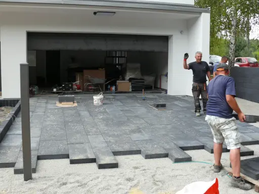 Pracownicy układają betonowe płyty, tworząc nowoczesny podjazd. Wygląda na to, że beton zamiast kostki to nowy trend.