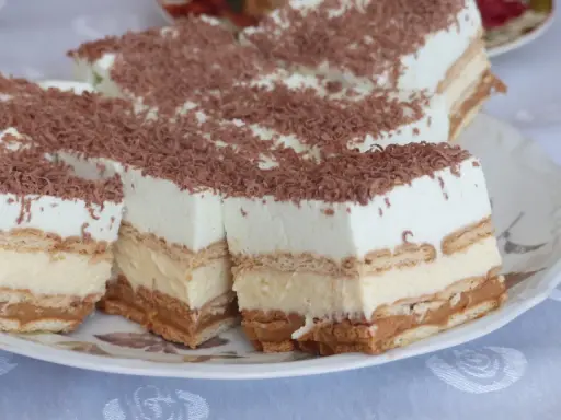 Szybkie ciasto bez pieczenia z budyniem i herbatnikami, udekorowane wiórkami czekolady. Idealne na deser!