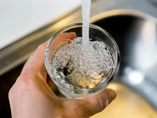 En hand håller ett glas som fylls med vatten från en kran. Bubblor bildas i vattnet, vilket kan tyda på klor i dricksvatten.