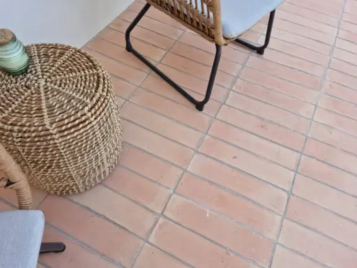 Suelo de baldosas de terracota con juntas limpias, listo para rellenar juntas baldosas suelo. Un cesto de mimbre y una silla de ratán completan la escena.