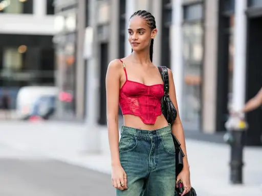 Frau mit geflochtenen conros Haare trägt ein rotes Korsett-Top und Jeans.