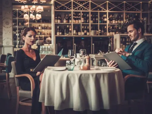 Elegancka para przegląda menu w luksusowej restauracji. On w granatowym garniturze, ona w czarnej sukni.