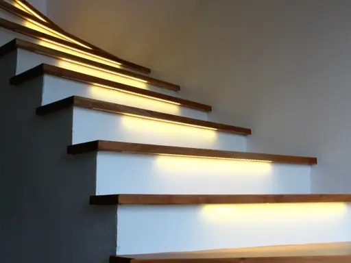 Nowoczesne lampy na klatkę schodową subtelnie oświetlają drewniane stopnie, tworząc ciepłą i bezpieczną atmosferę.